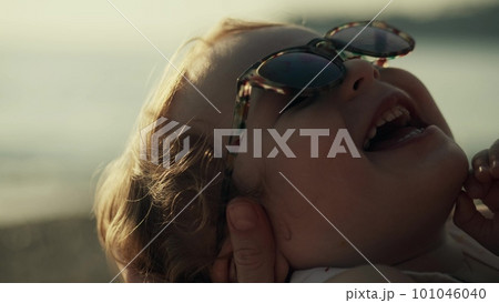Mother holds smiling little baby girl wearing sunglasses, close-up 101046040