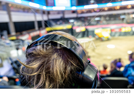 Selective focus on spectators in the stands with hearing protection watching a monster truck rally. Selective focus on spectators in the stands with hearing protection watching a monster truck rally. 101050583