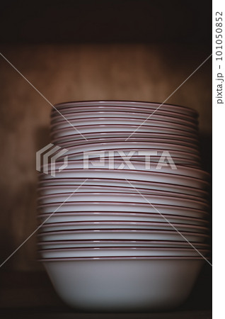Narrow depth of field picture of an open kitchen cabinet stacked ceramic plates and bowls. 101050852