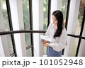 Young woman standing near the glass door and holding some notebooks 101052948
