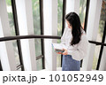 Young woman holding some notebooks near the glass door in the daytime 101052949