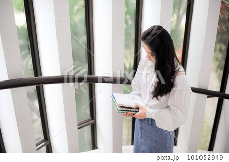 Young woman holding some notebooks near the glass door in the daytime 101052949