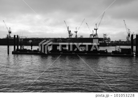 Grayscale of a floating cafe on the water before the cranes in the port of Hamburg Grayscale of a floating cafe on the water before the cranes in the port of Hamburg 101053228