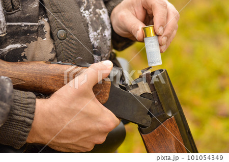 Selective focus of the hands of a man in a camouflage protective suit who loads a double-barreled shotgun. The concept of hunting. 101054349