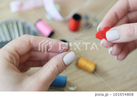 Hands of woman using special tool for threading blue needle Hands of woman using special tool for threading blue needle 101054808
