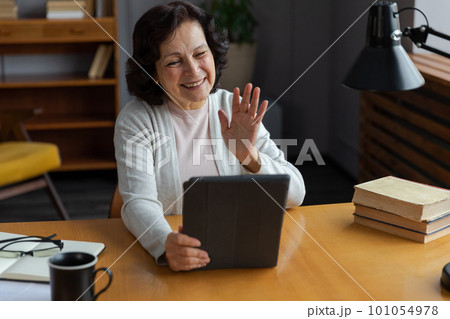 Happy middle aged senior woman holding tablet talk on video call with friends family. Laughing mature old senior grandmother having fun talking speaking with grown up children online 101054978