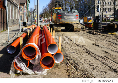 Street reconstruction site, stacked plastic sewage pipes, vertical well, excavator, dewatering pump 101055231