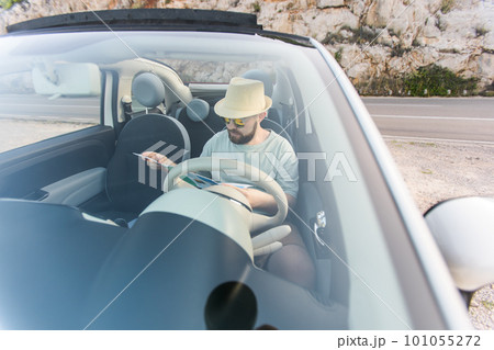 Hipster man looking on location navigation map in car, tourist traveler driving and hold in male hands europe cartography, view and plan tourist way road, trip in transportation cabriolet auto 101055272