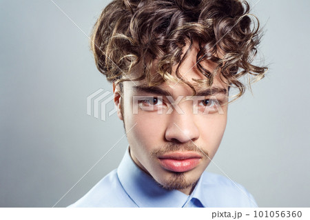 Portrait of handsome man with mustache and beard with curly hairstyle, wearing blue shirt, looking at camera with serious expression. Indoor studio shot isolated on gray background. Portrait of handsome man with mustache and beard with curly hairstyle, wearing blue shirt, looking at camera with serious expression. Indoor studio shot isolated on gray background. 101056360