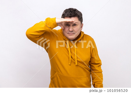 Thoughtful dark haired man looking far away at distance with hand over head, attentively searching for bright future, wearing urban style hoodie. Indoor studio shot isolated on white background. 101056520