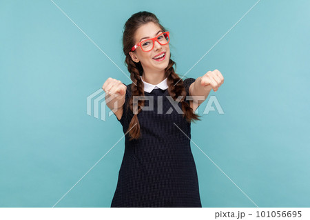 Portrait of smiling cheerful woman with braids pointing at camera indicating at you, making choice, wearing black dress and red glasses. woman Indoor studio shot isolated on blue background 101056695