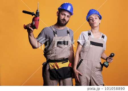 Man and woman renovators using drilling tools in studio, holding electric power drills for renovation work. Team of contractors working together on refurbishment project, using nail guns. Man and woman renovators using drilling tools in studio, holding electric power drills for renovation work. Team of contractors working together on refurbishment project, using nail guns. 101058890