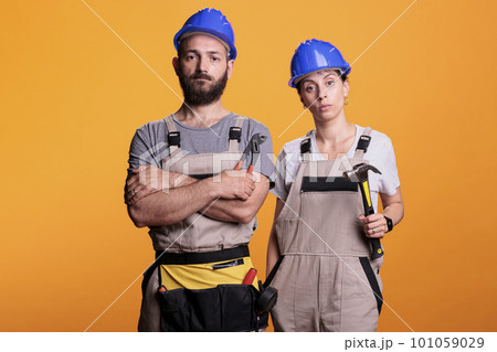 Team of building engineers holding renovating tools on camera, using sledgehammer and pair of pliers to work on renovation project. Builders posing with hammer and pliers over background. 101059029