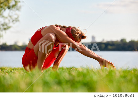 A woman is engaged in animal flow gymnastics, close-up outdoors near the river on green grass in red clothes. 101059031