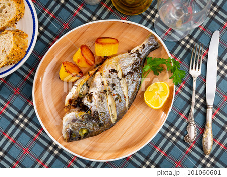 Baked in oven dorado fish with lemon and potatoes served on plate closeup 101060601