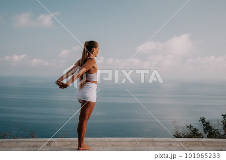 Fitness woman sea. A happy middle aged woman in white sportswear exercises morning outdoors in a park with a beach view. Female fitness pilates yoga routine concept. Healthy lifestyle. Fitness woman sea. A happy middle aged woman in white sportswear exercises morning outdoors in a park with a beach view. Female fitness pilates yoga routine concept. Healthy lifestyle. 101065233