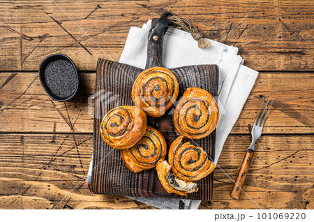 Poppy seed rolls and cardamom buns, Traditional Nordic baked sweet breads on wooden board. Wooden background. Top view Poppy seed rolls and cardamom buns, Traditional Nordic baked sweet breads on wooden board. Wooden background. Top view 101069220