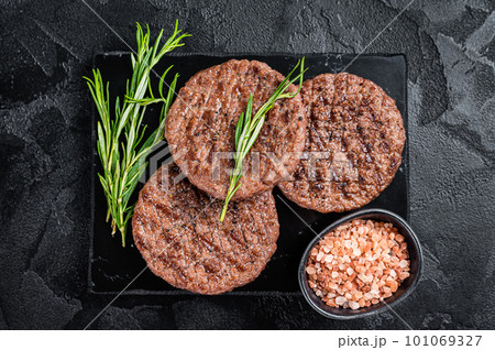 Beef burger patty cutlet for hamburger grilled on BBQ on marble board with rosemary. Black background. Top view 101069327