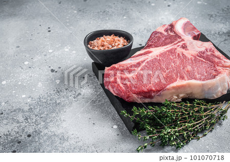 Raw dry aged wagyu porterhouse beef steak, uncooked T-bone on marble board with thyme. Gray background. Top view. Copy space 101070718