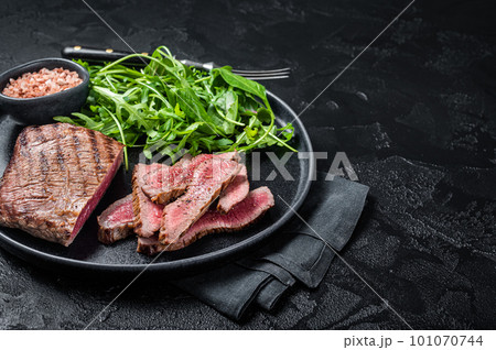 BBQ grilled Skirt Steak on a plate with green salad. Black background. Top view. Copy space 101070744