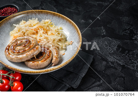 Roast bavarian spiral meat sausages on a plate with sauerkraut. Black background. Top view. Copy space Roast bavarian spiral meat sausages on a plate with sauerkraut. Black background. Top view. Copy space 101070764