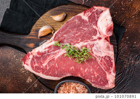 Raw Porterhouse steak, marbled beef meat on a wooden board. Dark background. Top view 101070891