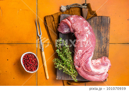 Fresh Raw pork tenderloin fillet meat on a wooden board with thyme. Orange background. Top view 101070939