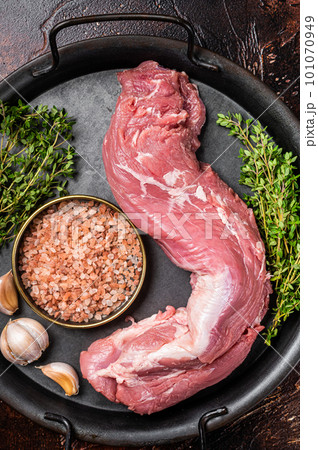 Uncooked Raw pork tenderloin fillet meat on a kitchet tray with thyme, garlic and sea salt. Dark background. Top view Uncooked Raw pork tenderloin fillet meat on a kitchet tray with thyme, garlic and sea salt. Dark background. Top view 101070949