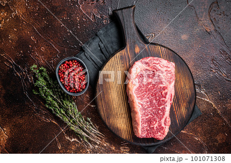 Uncooked Raw striploin or club steak on wooden board with thyme. Dark background. Top view Uncooked Raw striploin or club steak on wooden board with thyme. Dark background. Top view 101071308