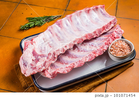 Fresh Raw pork spare loin ribs in a steel tray with herbs. Orange background. Top view 101071454