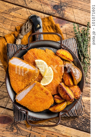 Delicious crispy pork schnitzel with fried potato wedges. Wooden background. Top view 101071601
