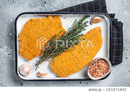 Cooking raw chicken schnitzel in breadcrumbs, uncooked meat steak. Gray background. Top view 101071602