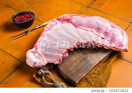 Raw rack of lamb mutton ribs on butcher board with spices. Orange background. Top view 101071611