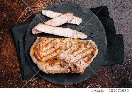 Roast BBQ pork Chop or T-bone meat steak sliced on a board. Dark background. Top view Roast BBQ pork Chop or T-bone meat steak sliced on a board. Dark background. Top view 101071620