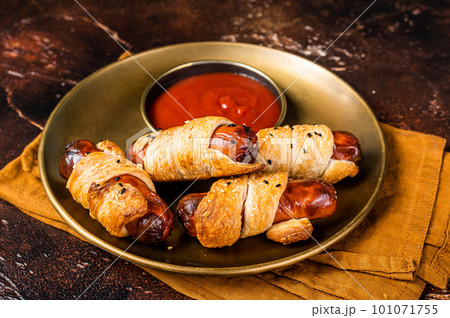 Rolled hot dog sausages baked in puff pastry with ketchup. Dark background. Top view Rolled hot dog sausages baked in puff pastry with ketchup. Dark background. Top view 101071755