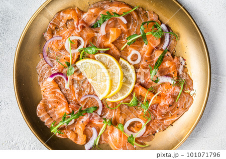 Fresh raw salmon carpaccio slices with onion and arugula served on a plate. White background. Top view Fresh raw salmon carpaccio slices with onion and arugula served on a plate. White background. Top view 101071796