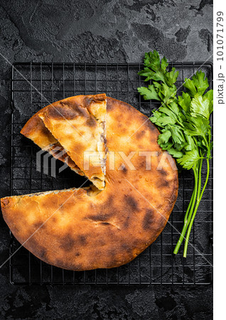 Baked Ossetian pie with beef meat and herbs. Black background. Top view Baked Ossetian pie with beef meat and herbs. Black background. Top view 101071799