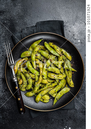 Stir-fried green Edamame Soy Beans with sea salt and sesame seeds in a plate. Black background. Top view 101071924