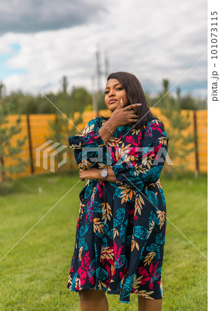 Summer portrait of beautiful african american woman in colourful dress wear standing on backyard. Suburban lifestyle and chilling on weekend in countryside and inclusion with diversity concept Summer portrait of beautiful african american woman in colourful dress wear standing on backyard. Suburban lifestyle and chilling on weekend in countryside and inclusion with diversity concept 101073115