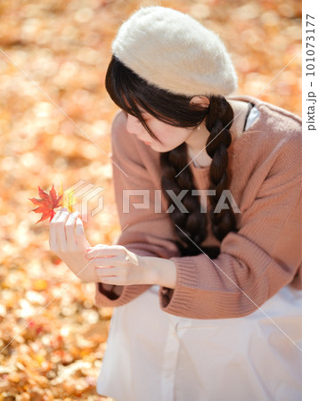 木漏れ日あふれる公園で紅葉を手にとる若い女性 木漏れ日あふれる公園で紅葉を手にとる若い女性 101073177