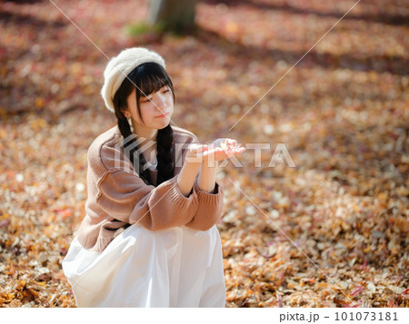 木漏れ日あふれる公園で紅葉を手にとる若い女性 101073181