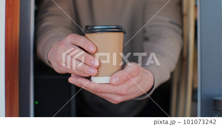 Close up male hand barista giving cup of coffee to camera and smiling. Barista handing drink coffee-to-go in cafe. Close up male hand barista giving cup of coffee to camera and smiling. Barista handing drink coffee-to-go in cafe. 101073242