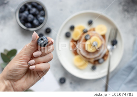 blueberries in female hand with beautiful nude manicure, over table with pancakes. blueberries in female hand with beautiful nude manicure, over table with pancakes. 101074783