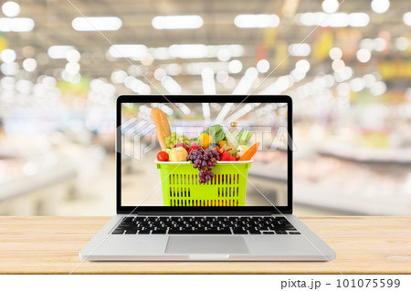 supermarket aisle blurred background with laptop computer and shopping basket on wood table grocery online concept 101075599