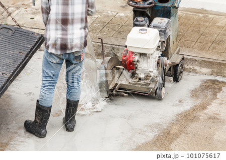 Worker using diamond saw blade machine cutting concrete road at construction site 101075617