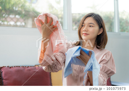 Happy young pragnent Asian woman in maternity clothes smiling and looking at a new baby clothes 101075973