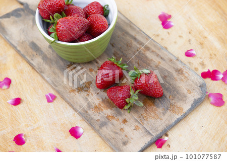 Above view of wet wooden board with bowl with strawberries and three strawberries lying on table. Concept of summer. 101077587