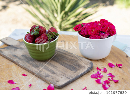 Front view of beautiful layout with stylish board with bowl with strawberries on wooden table with petals. Concept of summer. Front view of beautiful layout with stylish board with bowl with strawberries on wooden table with petals. Concept of summer. 101077620