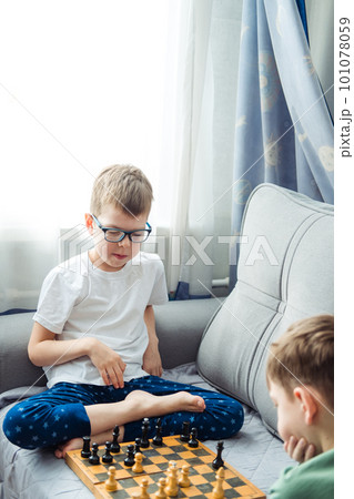 Boys playing wooden chess lying on a gray sofa in front of the window Boys playing wooden chess lying on a gray sofa in front of the window 101078059