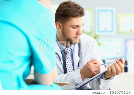 Male doctor looks at patient medical record in clinic 101079119